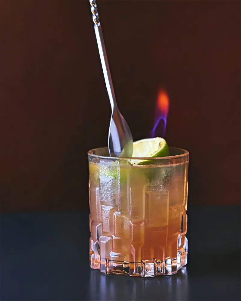 Cocktail con bar spoon e fiamma su fondo scuro