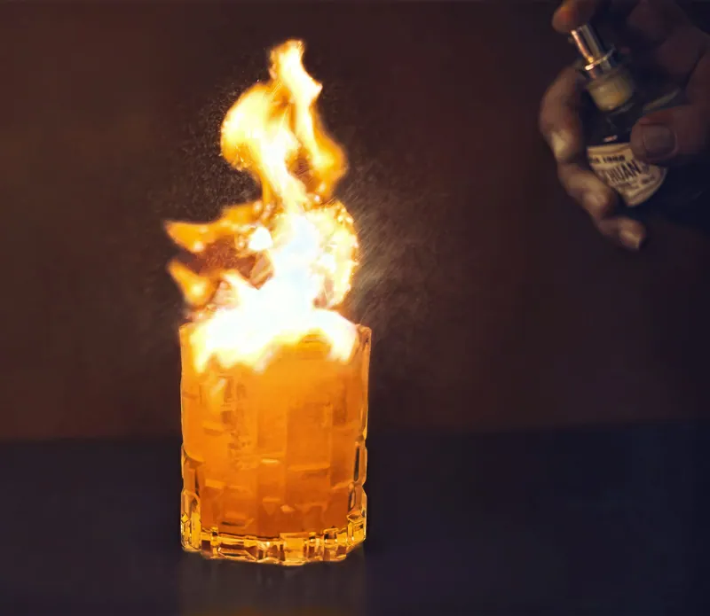 Cocktail in bicchiere basso avvolto da una fiammata su fondo scuro