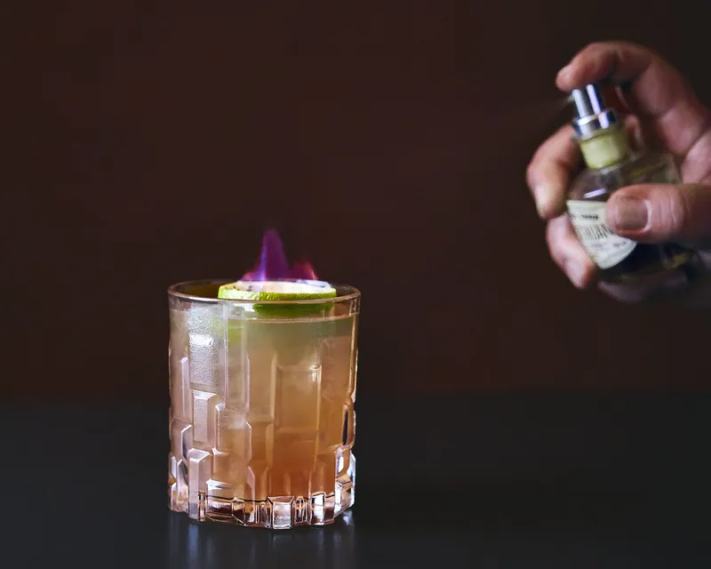 Cocktail profumato con nebulizzatore su fondo scuro