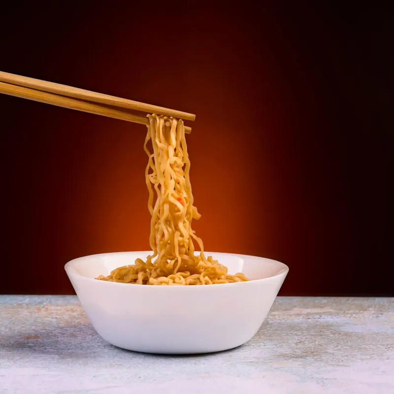 Noodles sollevati con le bacchette su fondo arancio scuro