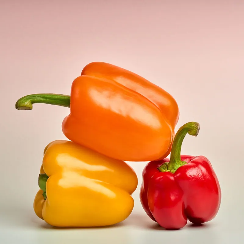 Peperoni arancione, giallo e rosso su fondale rosa