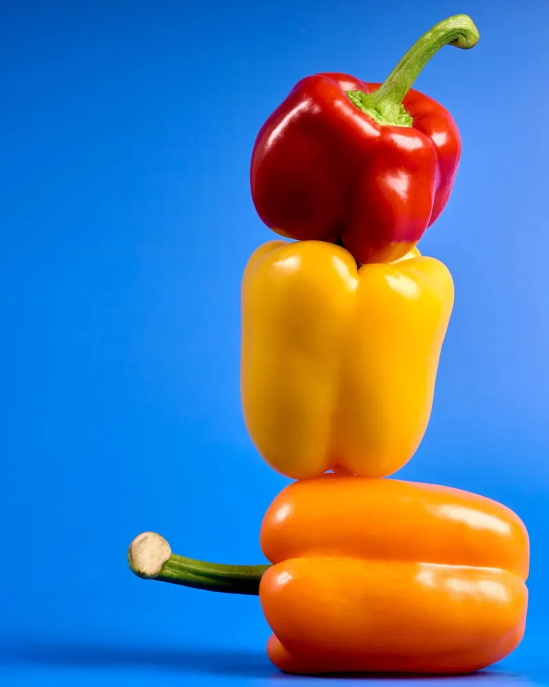 Peperoni rosso, giallo e arancione impilati su fondale blu