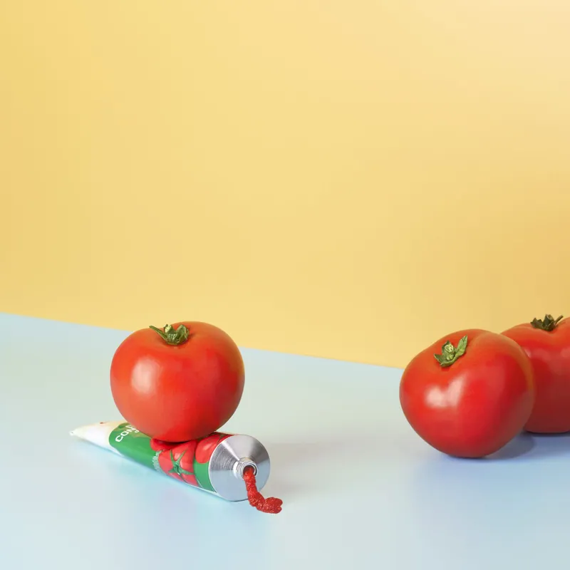 Pomodori e tubetto di concentrato su fondo giallo e azzurro