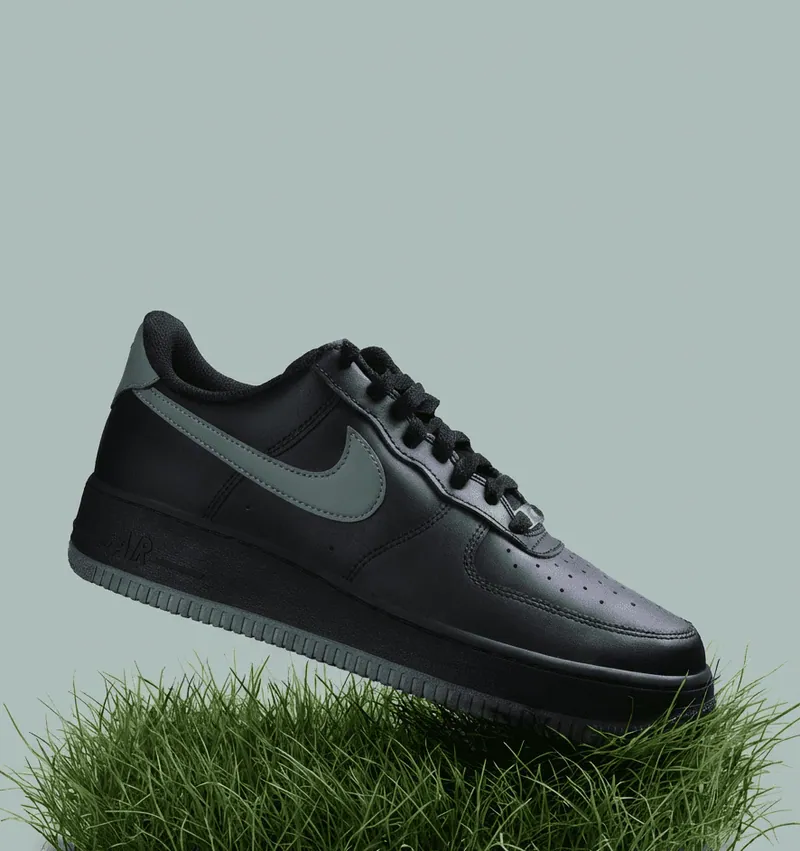 Sneaker nera con logo verde salvia sospesa sopra un ciuffo d’erba su sfondo verde chiaro.