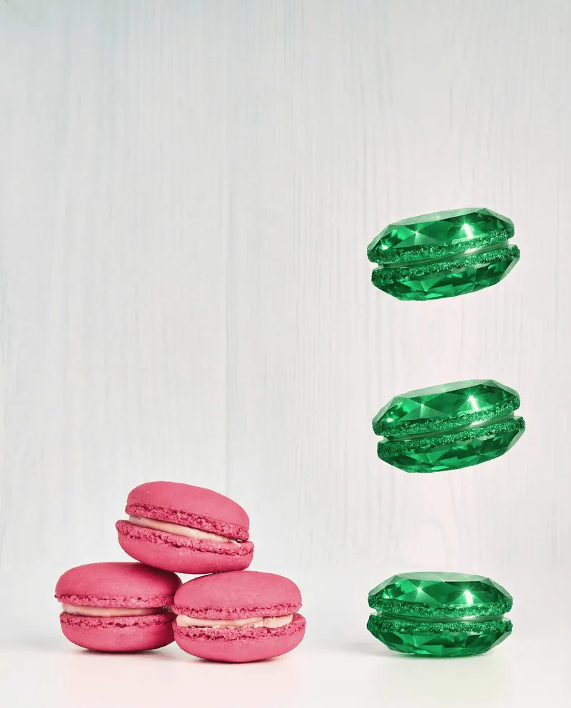 Tre macaron rosa appoggiati e macaron verdi effetto gemma sospesi su sfondo chiaro.
