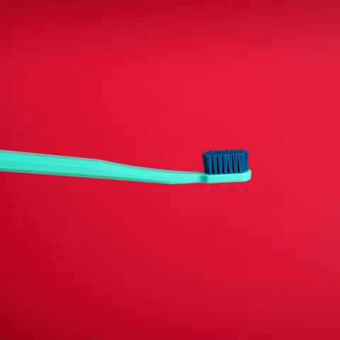 Spazzolino turchese sospeso su fondale rosso